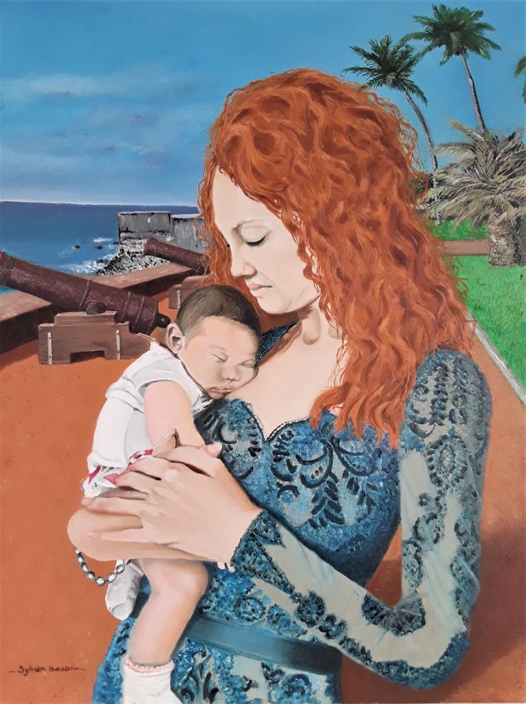 Jeune maman tenant dans ses bras sa petite fille en bas âge. On reconnait le promontoir du Barachois à Saint Denis de la Réunion dans l'arrière plan.