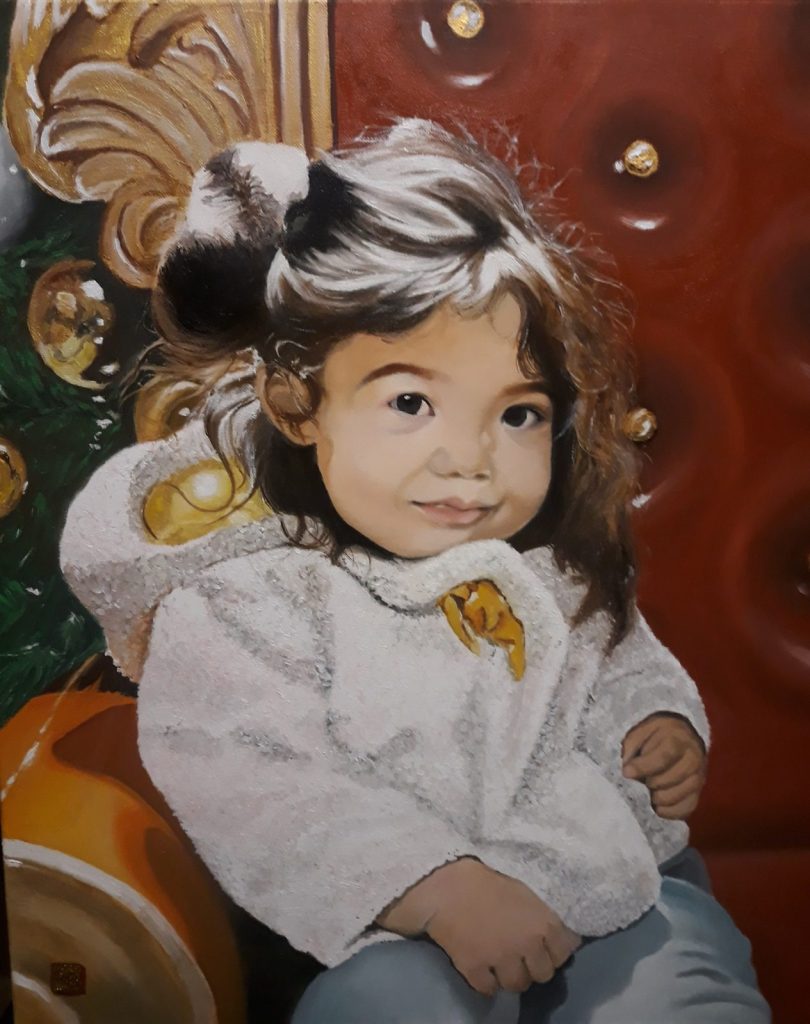 Naia assis dans le fauteuil du Père Noël. Pleine de candeur et tout sourire. Un éclairage au dessus de sa tête apporte un éclat particulier sur ses cheveux bruns.